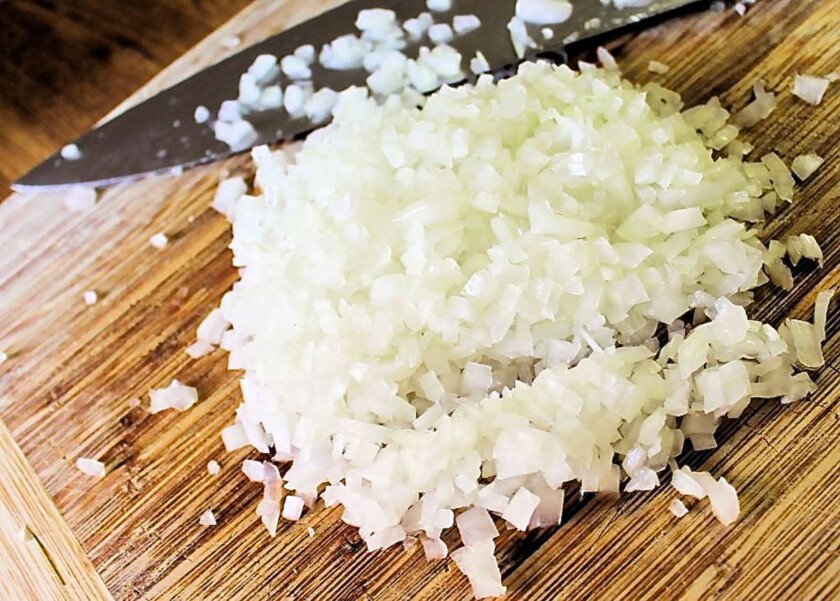 Cebollas picaditas con un cuchillo en un tabla de cortar.