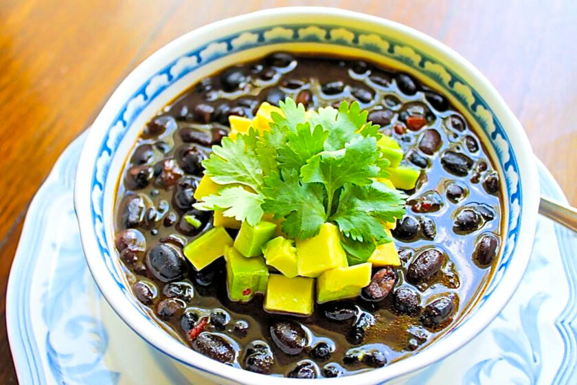 Bol de sopa de caraotas negras con un topping de aguacate con cilantro.
