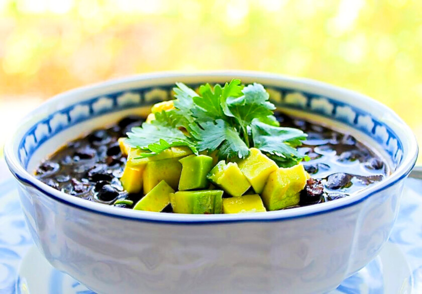 Un tazón de sopa de caraotas negras con aguacate y cilantro fresco.