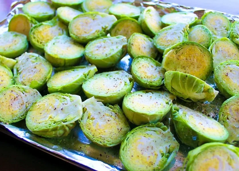 Halved Brussels sprouts are spread out on a baking sheet lined with aluminum foil, seasoned with salt and pepper, and ready to be roasted for delicious Roasted Brussels Sprouts. Try adding cranberries for a sweet twist!.
