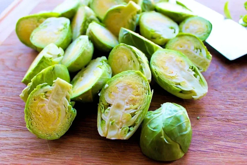 Halved and whole Brussels sprouts are displayed on a wooden cutting board, ready to be transformed into delicious roasted Brussels sprouts with a hint of balsamic reduction. A knife is partially visible in the background.