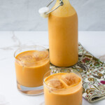 Dos vasos de Ponche crema de calabaza sobre una mesa junto a una botella.