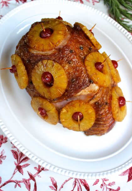 A roasted ham with pineapples and cherries on a plate.