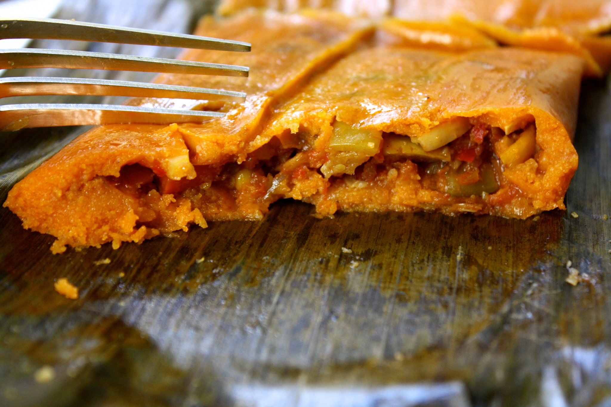 A vegetarian hallaca, serve on aplantain leaf, already cut. There is a fork too.