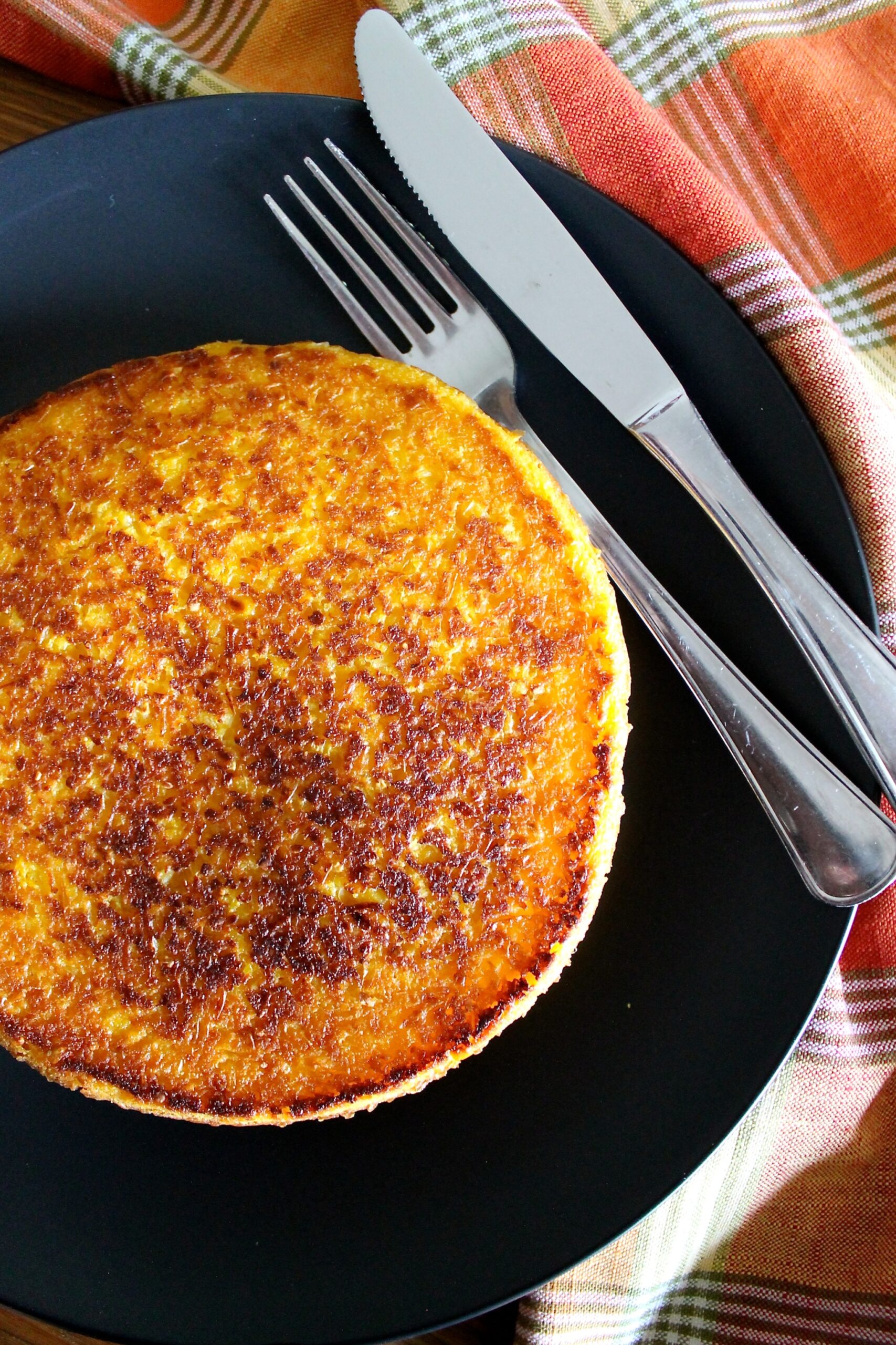 Cachapa con queso de mano servida en un plato negro. Al lado hay un cuchillo y un tenedor.