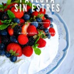 Una pavlova de frutas del bosque cubierta con fresas, arándanos, moras y hojas de menta. El texto superpuesto en español dice: "CÓMO HACER PAVLOVA SIN ESTRÉS - Receta fácil y deliciosa.