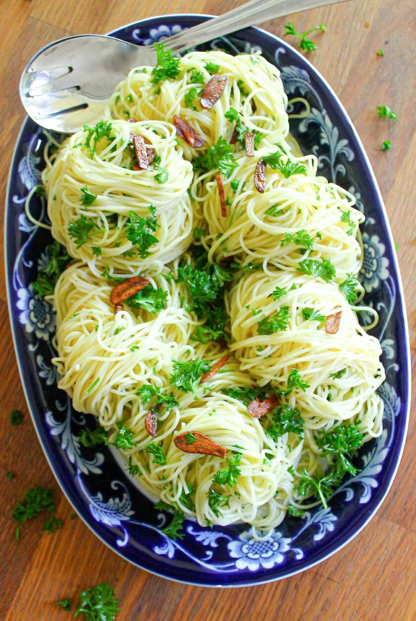 Capellini aglio y olio with parsley on a blue oval serving dish.