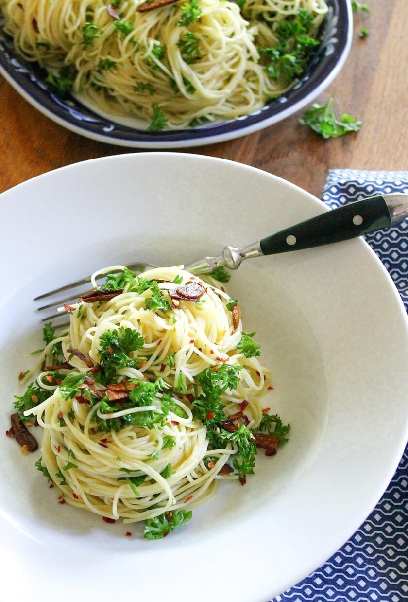 Aglio e olio capellini with peperoncino and parsley, served in a pasta bowl with a fork.