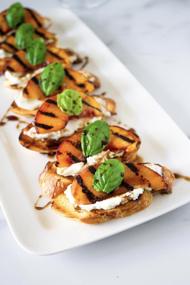 Grilled peach chèvre bruschetta served on a white plate.