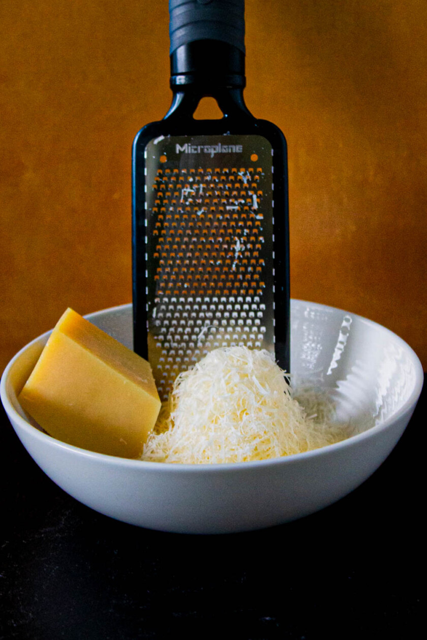 Un bol de queso y un rallador de queso, hay un pedazo de queso parmesano, by enrilemoine.