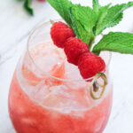 Raspberry mojito in glass garnished with a raspberry skewer and a sprig of spearmint.