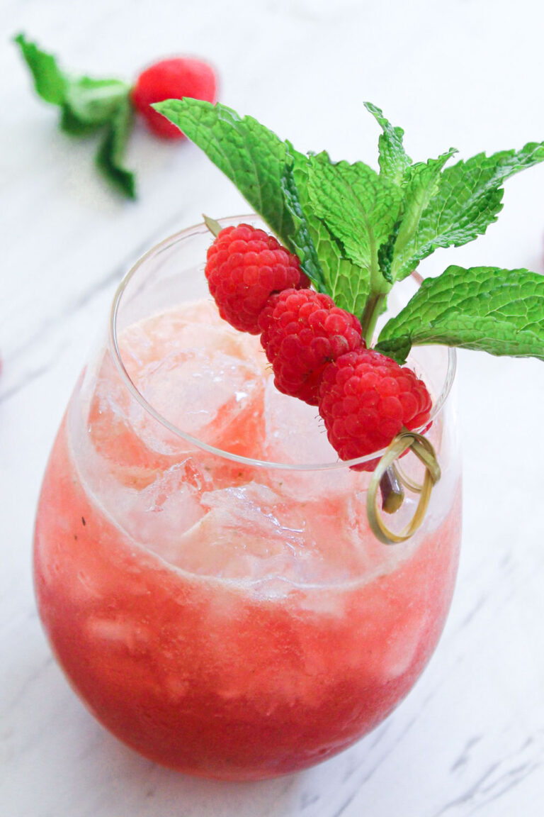 Raspberry mojito in glass garnished with a raspberry skewer and a sprig of spearmint.