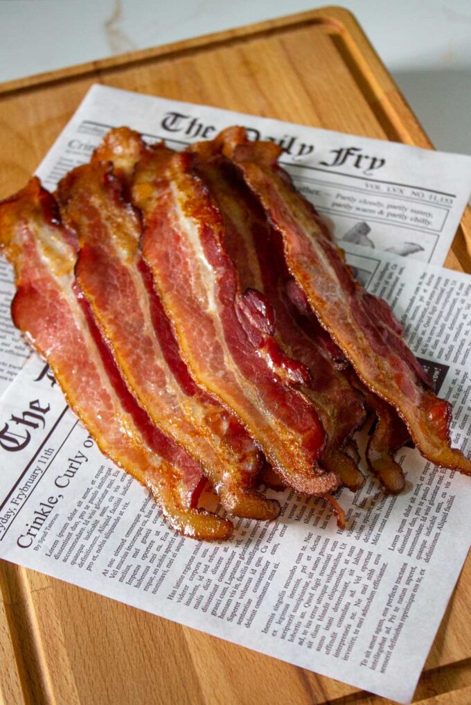 Bacon slices, cooked to perfection and placed over deli paper simulating newspaper.