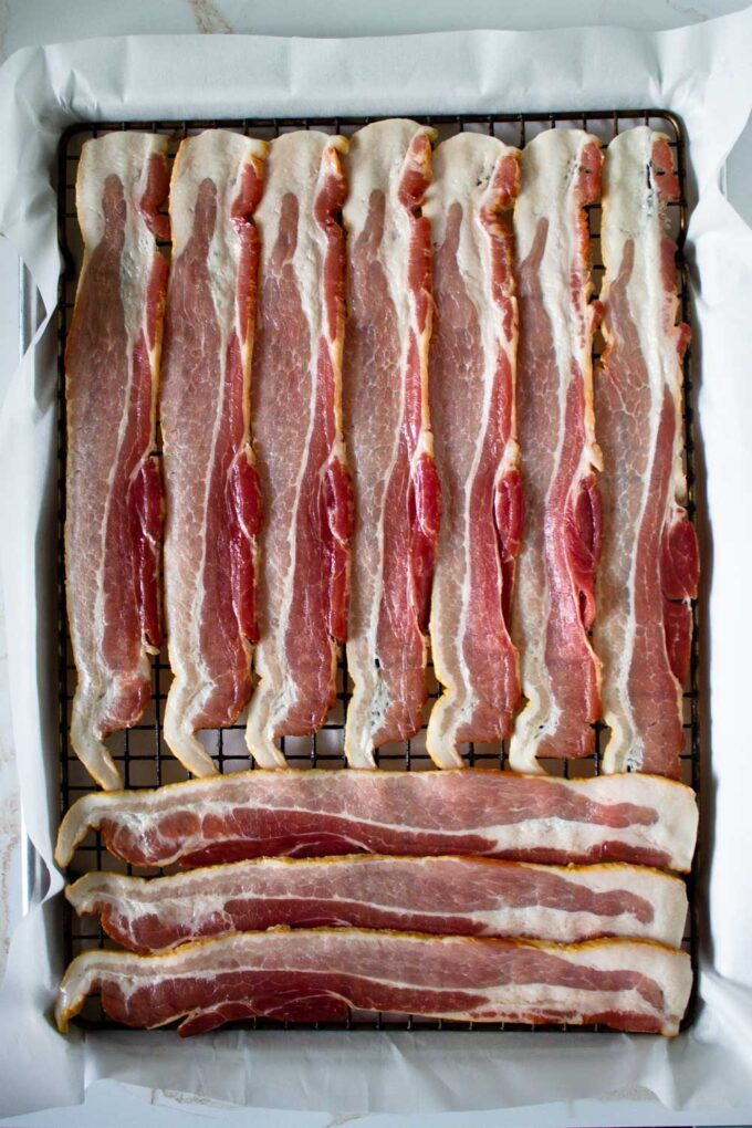 Uncooked bacon slices arranged on top of a rack on a baking sheet.