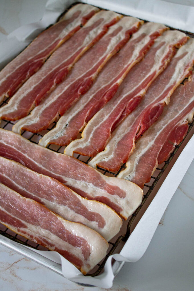 Uncooked bacon slices on a baking tray before been oven-baked to perfection.