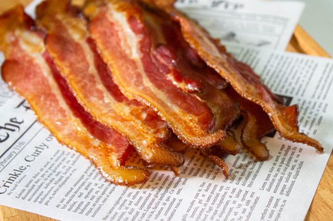 Bacon slices cooked to perfection in the oven. The bacon in place on deli paper that simulates a newspaper.