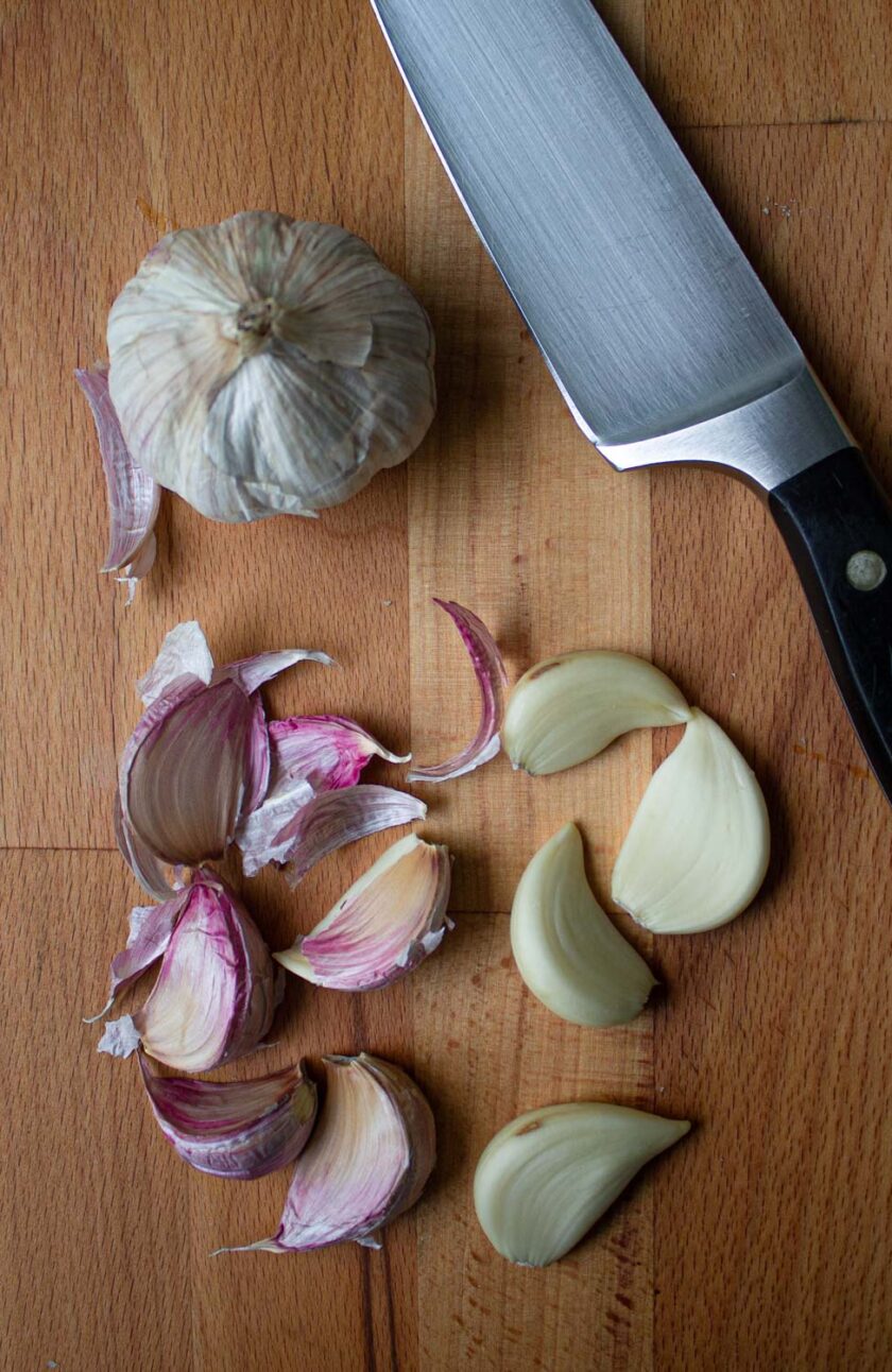 Garlic bulb, and garlic cloves on a cutting board with a knife.