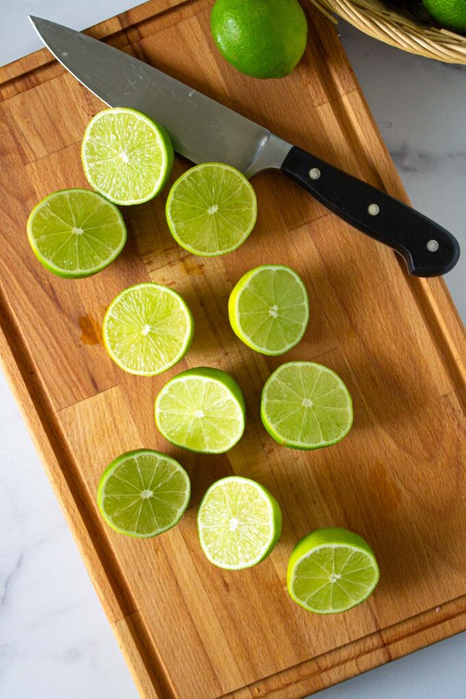 Limones verdes o limas cortados en dos, sobre una tabla de madera, by enrilemoine.
