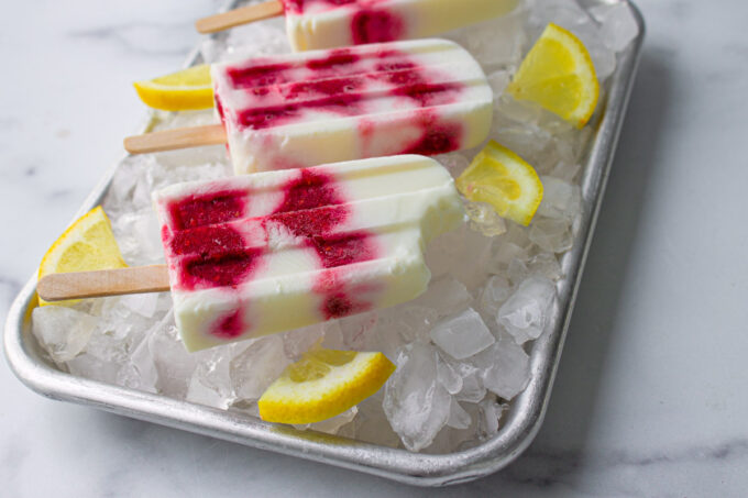 Primer plato de paletas de helado de yogurt con frambuesas y limón, puestas sobre una bandeja con hielo, by enrilemoine.