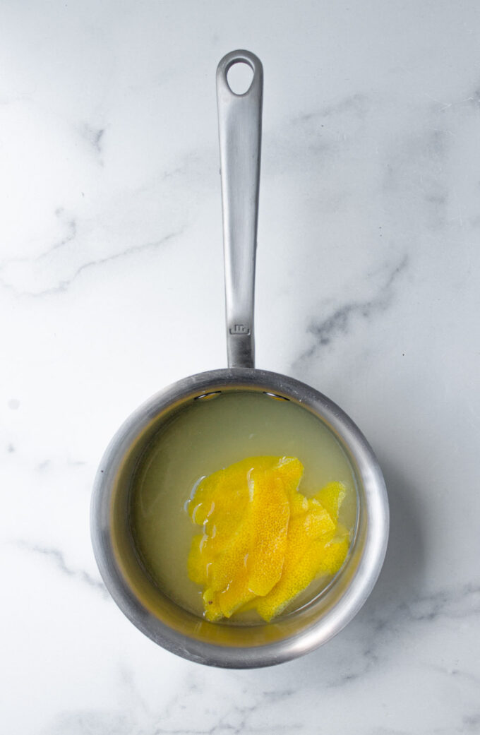 Olla pequeña de acero con los ingredientes para hacer jarabe de limón, incluyendo jugo de limón, azúcar y piel de limón, by enrilemoine.