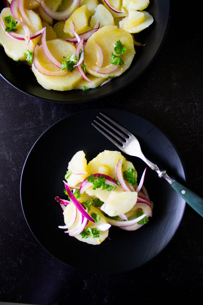 Venezuelan potato salad served in a black dish. There is also a platter with more salad too, by enrilemoine.