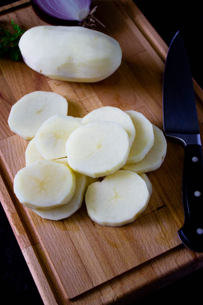 Sliced potatoes on a wooden cutting board to make Venezuelan potato salad, by enrilemoine.
