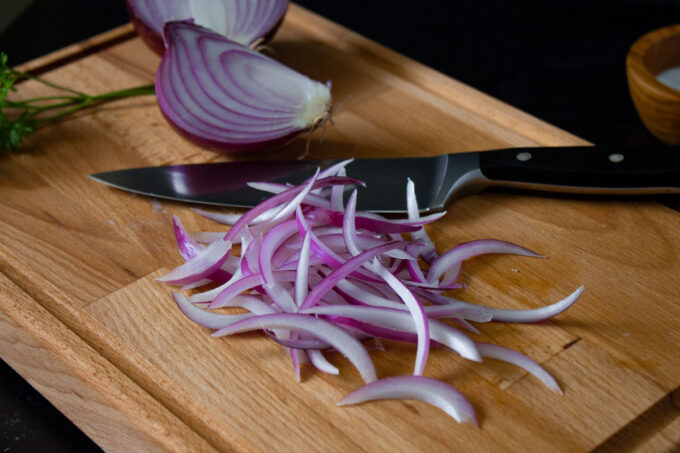 Red onions cut in julienne on a wooden cutting board, to make Venezuelan potato salad.
