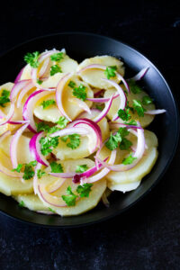 Ensalada de papa venezolana, servida en un plato negro, by enrilemoine.