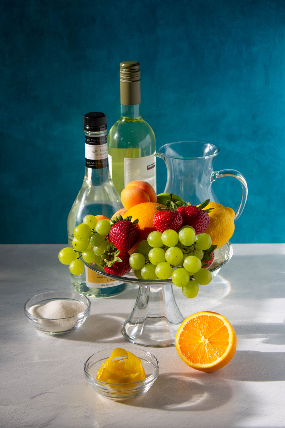 Ingredientes para hacer sangría de vino blanco, incluyendo, además del vino, triple sec, azúcar, piel de limón, y fruta fresca.