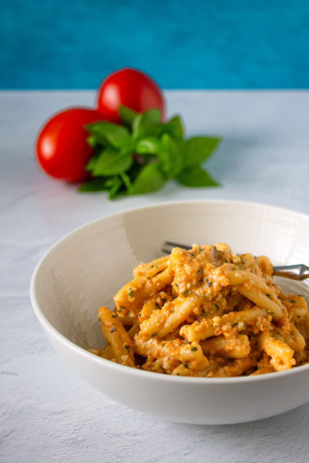 Bol de pasta con pesto alla Trapanese, al fondo se ven unos tomates y una albahaca, by enrilemoine.