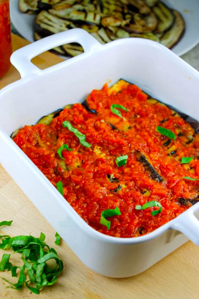 El proceso de preparar una lasaña con capas de berenjena y de salsa de tomates, además a hojas frescas de albahaca, by enrilemoine.