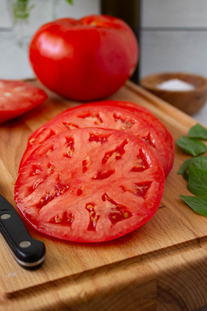 Close up of a beefsteak tomato sliced, there is a whole tomato too, by enrilemoine.