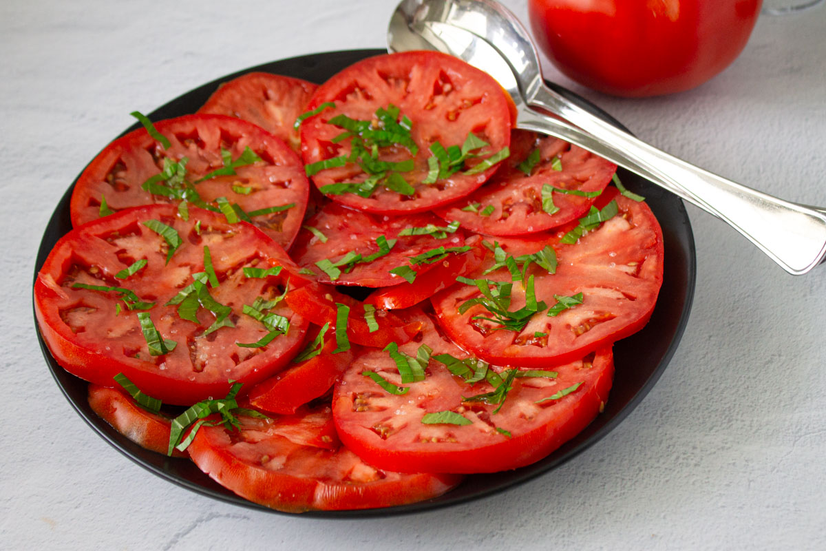Rodajas de tomate en un plato con una cuchara en una ensalada de tomate y albahaca, by enrilemoine.