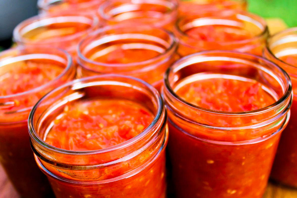 Jars of tomato sauce on a wooden cutting board used in preparing Venezuelan tomato & onion Sofrito, by enrilemoine.