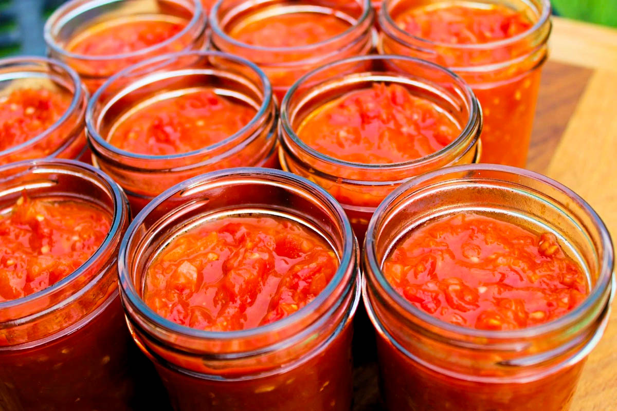 Five jars of tomato sauce and a wooden cutting board.