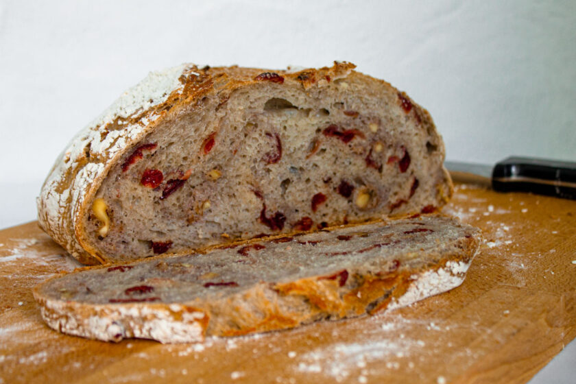 Una hogaza de pan con arándanos y nueces, rebanada dobre una tabla de madera, by enrilemoine.