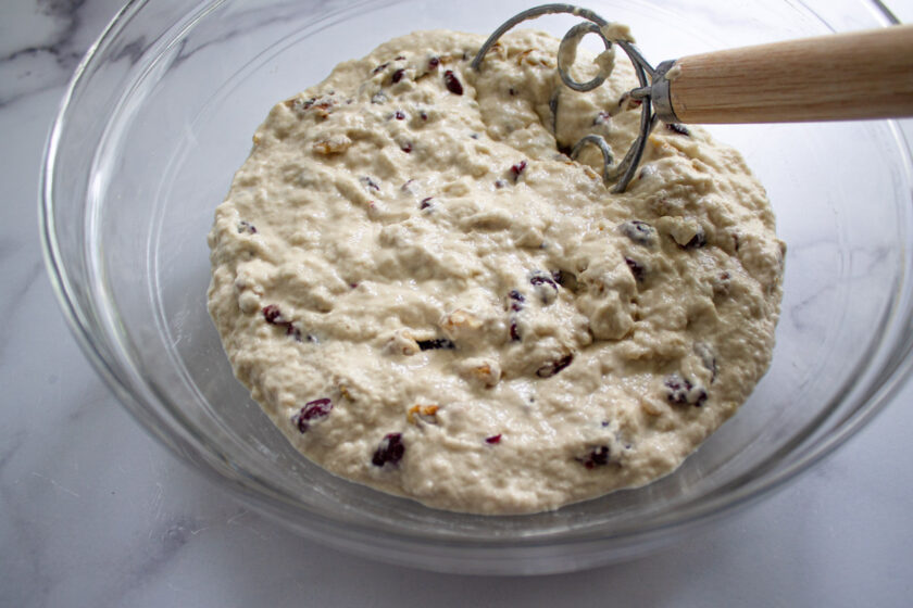 Un bol de masa cruda con arándanos y nueces, con un batidor danés, by enrilemoine.