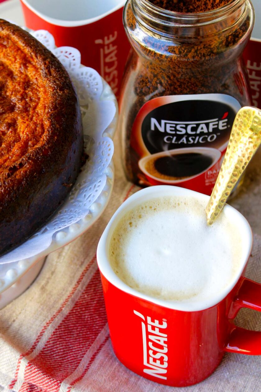 Una taza de café en una mesa junto a una torta de jojoto.