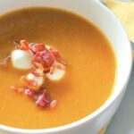 Un plato de sopa de vegetales asados con tocino y queso.