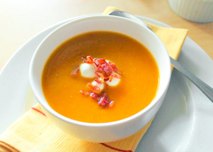 A bowl of soup with bacon on top.