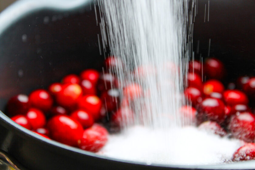 Sugar being added to a pot with fresh cranberries.