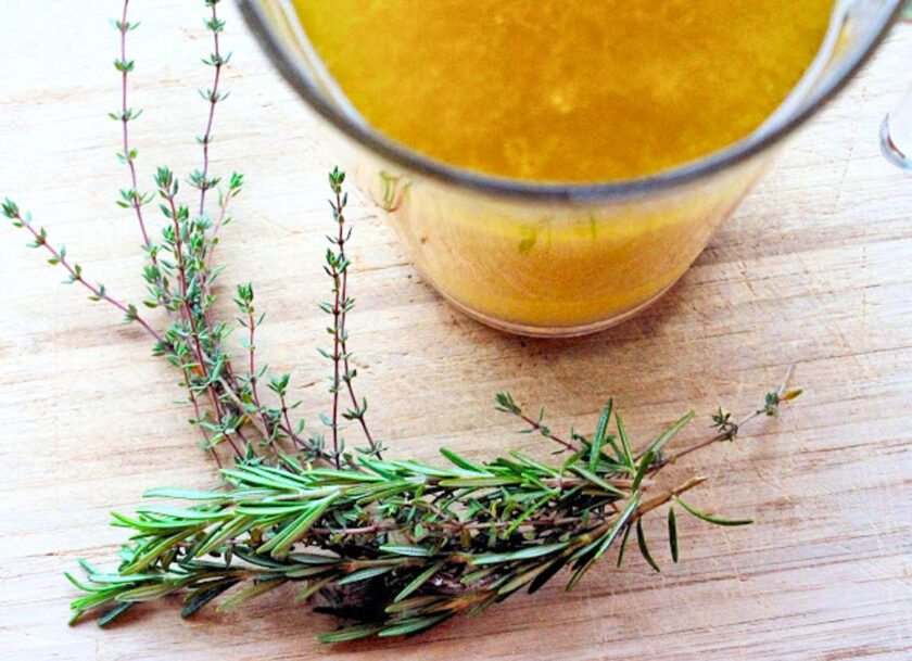 A jar with turkey drippings and a fresh thyme and rosemary sprigs over a wooden board, by enrilemoine.