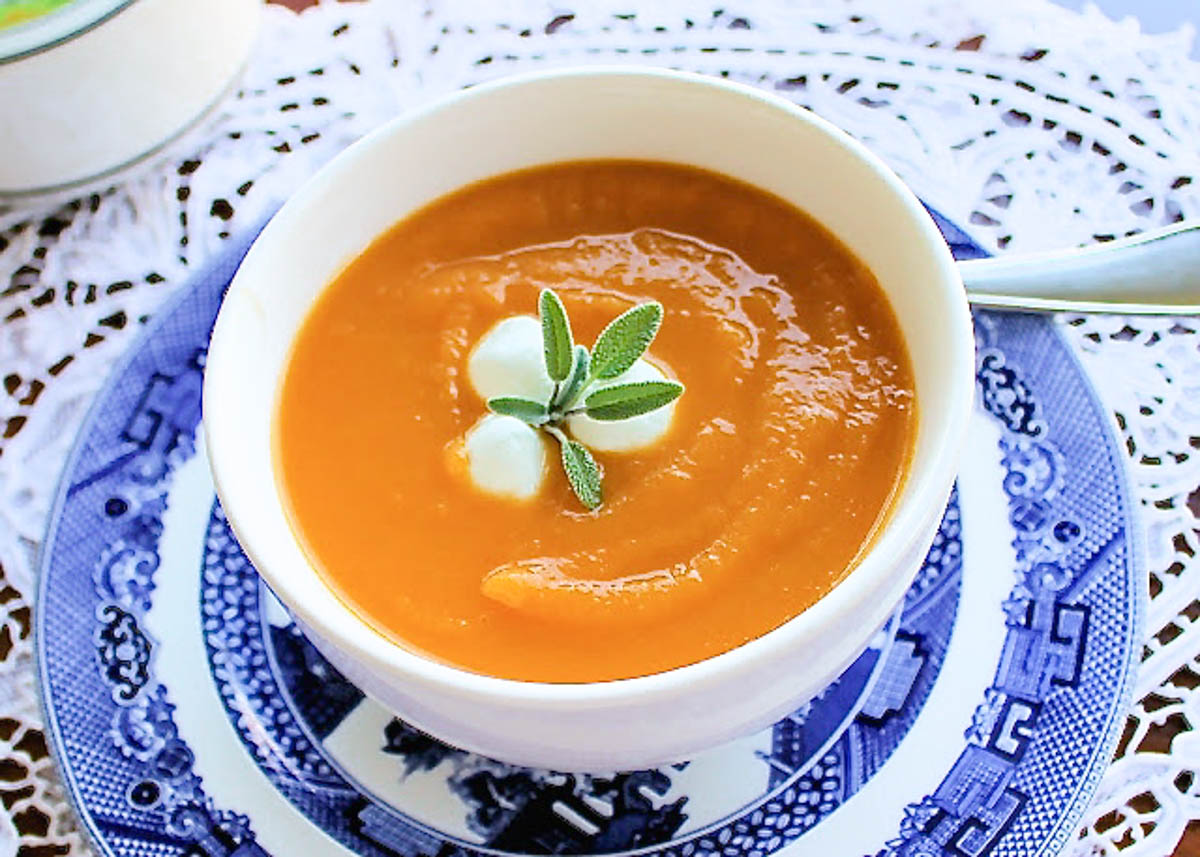 A bowl of butternut squash and sweet potato creamy soup, garnished with fresh sage.