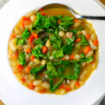A warm, cozy white plate with a bowl of cannellini minestrone with chards.