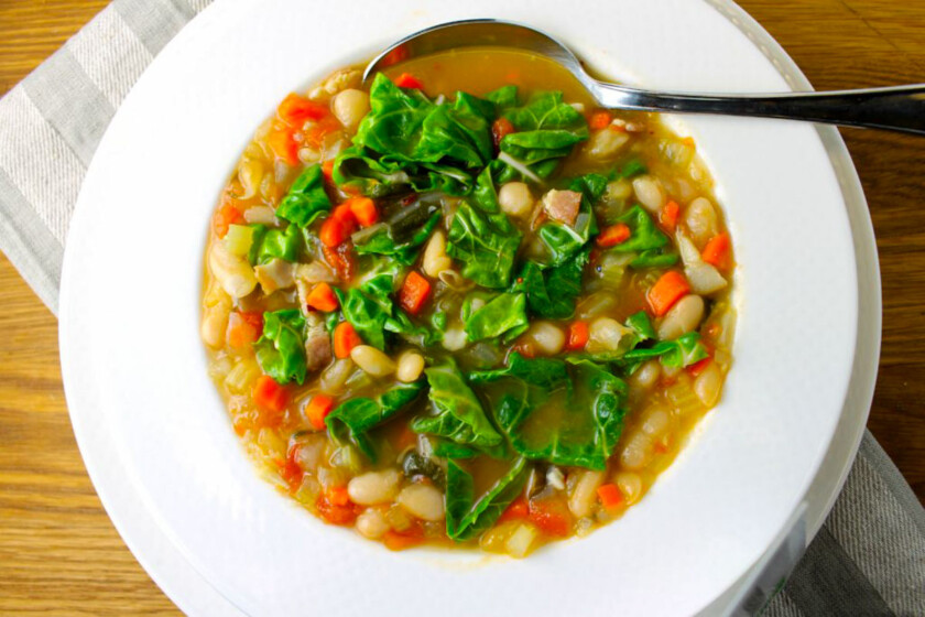 A warm, cozy white plate with a bowl of cannellini minestrone with chards.
