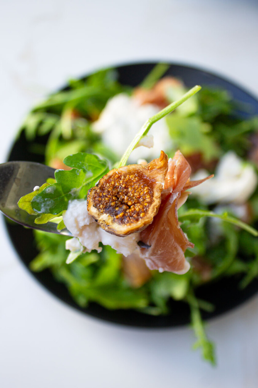 Un tenedor sostiene una ensalada con higos y prosciutto.