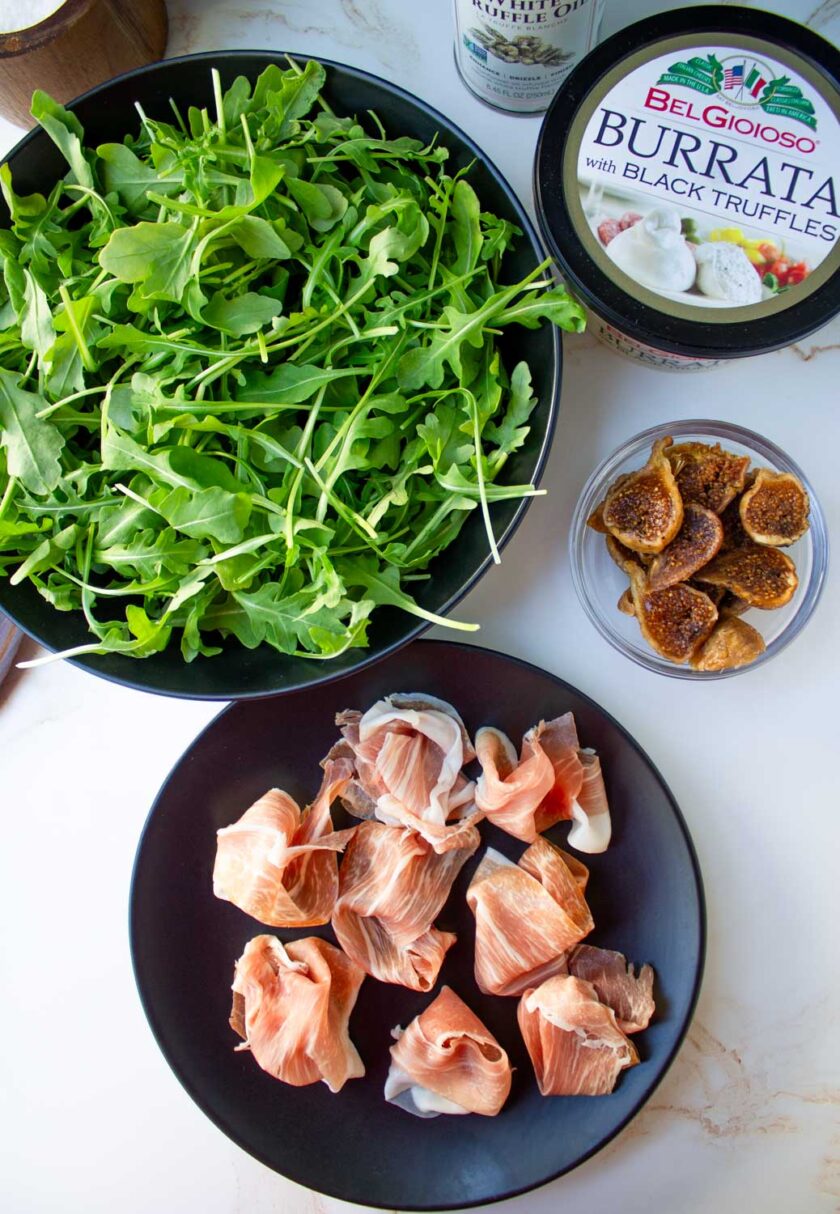 Ingredientes para hacer ensalada de rúcula, burrata, higos secos y prosciutto.