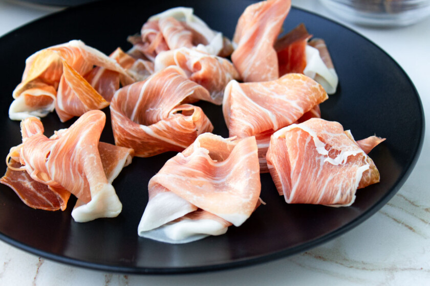 Rebanadas de prosciutto di Parma en un plato negro.