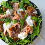 Ensalada de hugos, prosciutto, burrata y arugula en una ensaladadera negra.