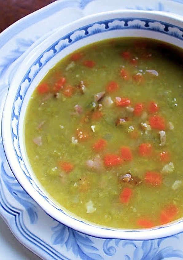 A bowl of green pea soupwith ham and carrtos.